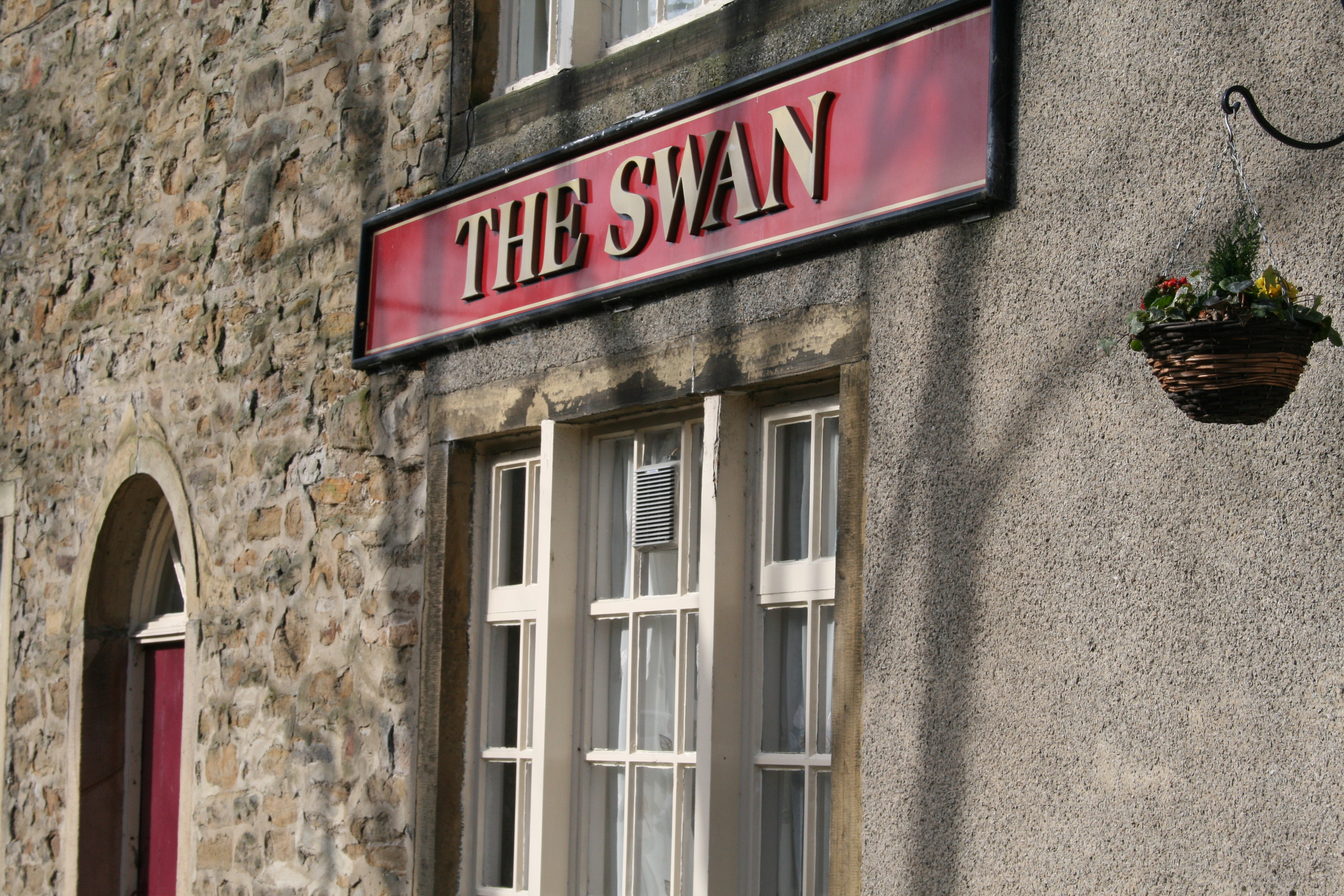 The Swan pub sign in Carleton, North Yorkshire, displayed in red on a stone building.