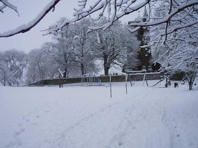 Snowy village park with playground and church in Carleton, North Yorkshire